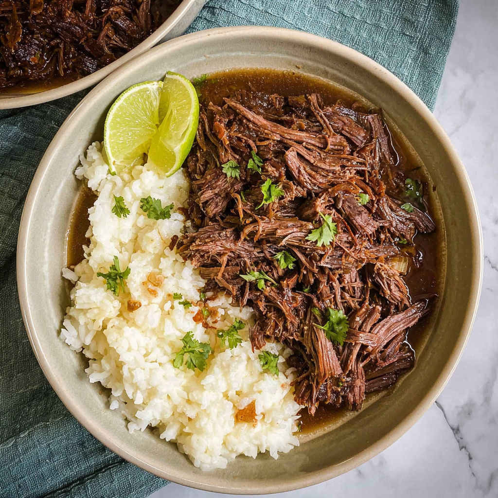 A bowl of beef stew with rice and lime wedges.