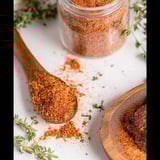 A jar of homemade blackening seasoning with a wooden spoon inside.