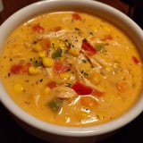 A bowl of soup with chicken and corn.