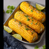 A pan of corn on the cob with lime wedges.