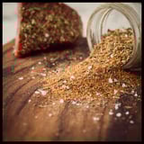 A jar of seasoning sits next to a piece of steak.