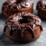 Three chocolate doughnuts with chocolate drizzle.