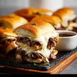 French dip sliders on a black cutting board.