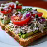 A sandwich with tuna, tomatoes, onions, and avocado.