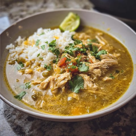 A bowl of chicken chili verde with rice and lime.