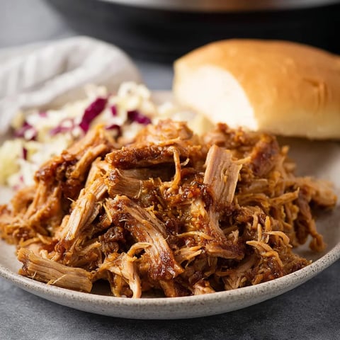 A plate of pulled pork with a roll and coleslaw.