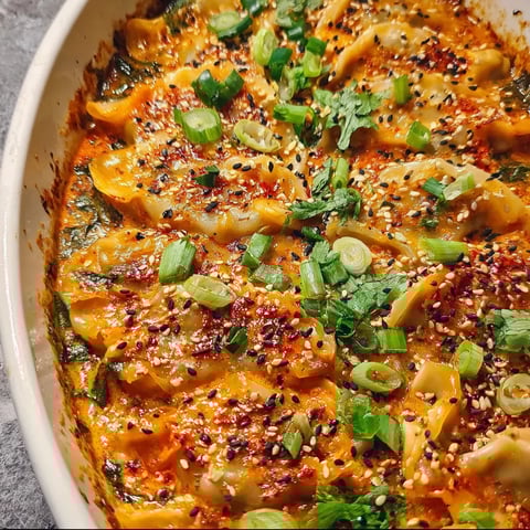A dish of baked dumplings with green onions and sesame seeds.
