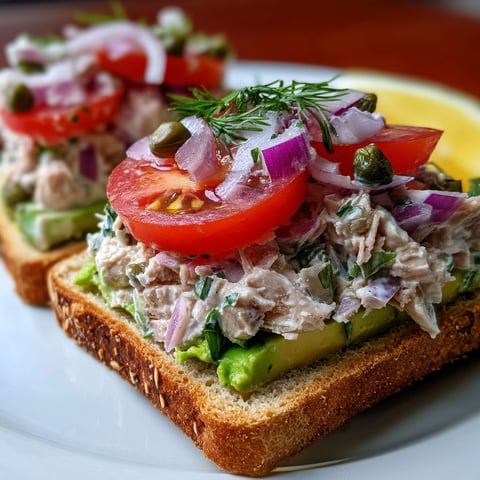 A sandwich with tuna, tomatoes, onions, and avocado.
